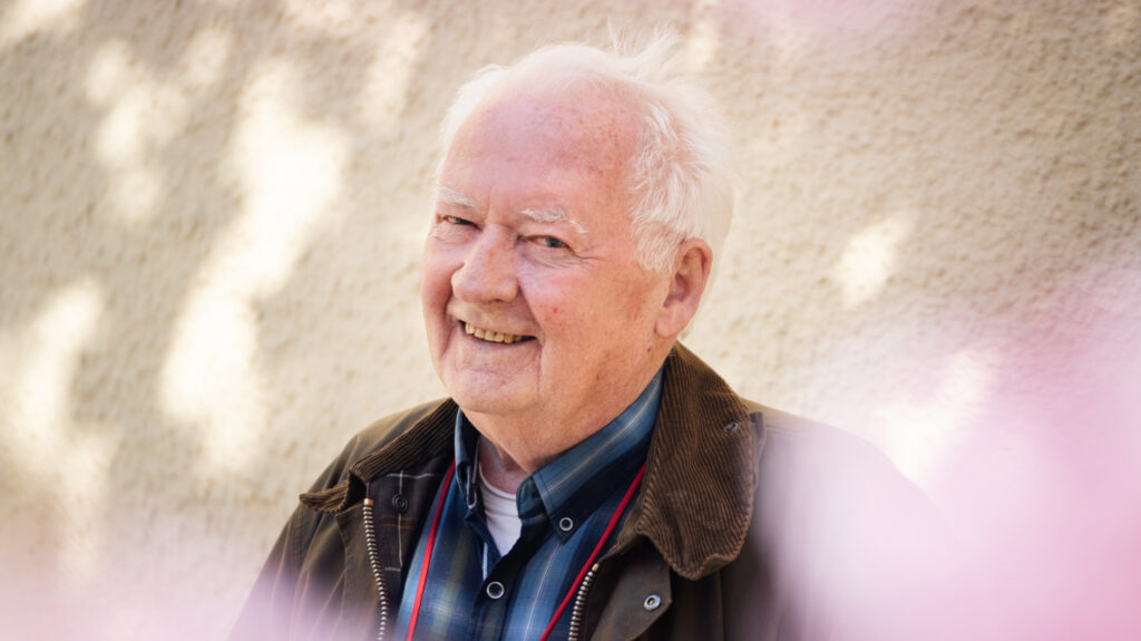 Rolf Åhrberg står framför en husvägg och i förgrunden finns rosa körsbärsblommor.